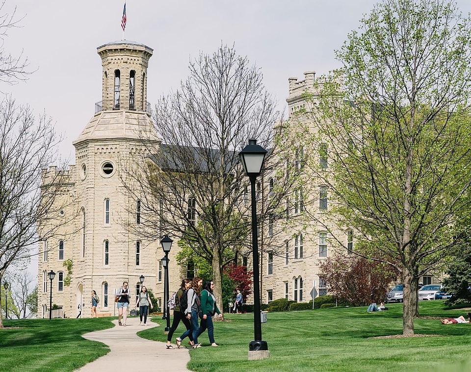 A white campus building with sidewalks leading up to it through a grassy commons.